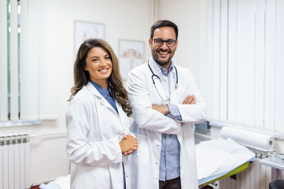 Dos médicos jóvenes sonrientes en consultorio, representando a profesionales de la salud que gestionan su práctica con ayuda de un software médico como HiMed.